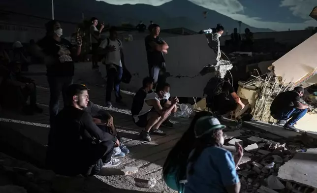 Residents watch rescuers' efforts to reach survivors beneath the rubble of a building that collapsed in the earthquakes in La Guaira, Venezuela, early Monday, June 29, 2026. (AP Photo/Matias Delacroix)
