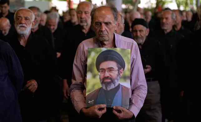 Iranian worshippers listen to the sermon of the Friday prayers as one of them holds a poster of the Supreme Leader Ayatollah Mojtaba Khamenei at the Tehran University campus in Tehran, Iran, Friday, June 19, 2026. (AP Photo/Vahid Salemi)