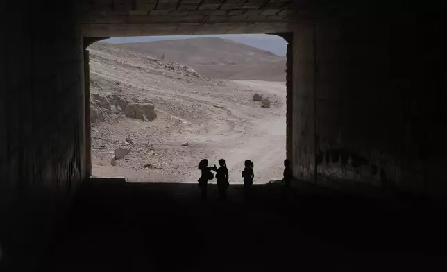 Palestinian children go through a vehicles tunnel on their way home, after receiving their year end reports from their school, in the West Bank Bedouin hamlets of Khan al-Ahmar, Wednesday, June 10, 2026. (AP Photo/Mahmoud Illean)