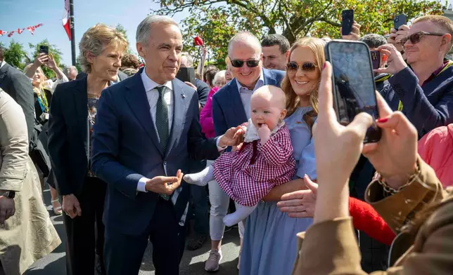 Canadian Prime Minister Mark Carney, front left, has a picture taken with Lily Meskil, 9 months and her grandfather Ger Basquel and mother Rachel Basquel, during a visit to Aughagower, Ireland, Sunday, June 14, 2026. (Andrew Downes/PA via AP)