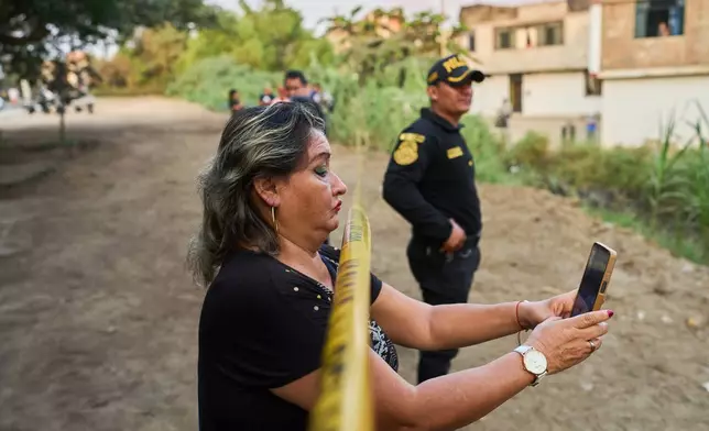A neighbor records the scene with a cellphone as police recover the body of Jose Perez from a ravine where he was found shot in Trujillo, Peru, Friday, May 30, 2026. (AP Photo/Rodrigo Abd)