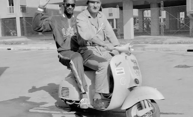 FILE - U.S. high jumper John Thomas, of Cambridge, Mass., waves from a Vespa scooter with an unidentified official Olympic driver inside the Olympic Village, in Rome, Aug. 27, 1960. (AP Photo/Mike Stern, File)