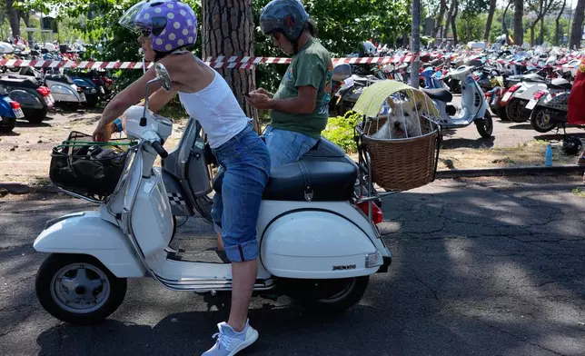 Natalie Dunand, a Vespa enthusiast from France, carries her dog Roxane as she arrives at the Vespa Village during celebrations for the 80th anniversary of the Vespa scooter in Rome, Thursday, June 25, 2026. (AP Photo/Alessandra Tarantino)