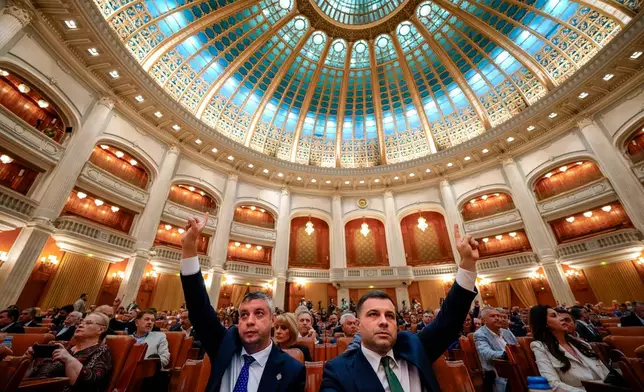 Romanian lawmakers raise their hands at the start of a joint parliament session ahead of a vote of confidence for the new government team led by Romanian Prime Minister designate Adrian Vestea, in Bucharest, Romania, Monday, June 22, 2026. (AP Photo/Vadim Ghirda)
