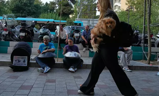 Street musicians play music as a woman carries a dog on a sidewalk in northern Tehran, Wednesday, June 10, 2026. (AP Photo/Vahid Salemi)