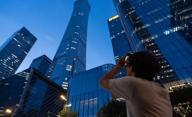 A passerby tries to take photo of the damage on the Citic Tower also known as Zun Tower in Beijing, China, Friday, June 26, 2026. (AP Photo/Han Guan Ng)