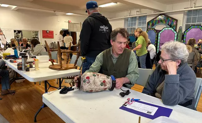 Wood repair coach Erik Hoover helps fix a lamp at a Repair Café in New Paltz, N.Y., May 23, 2026. (AP Photo/Michael Weissenstein)