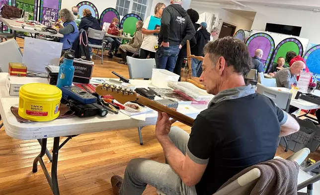 Music repair coach James Dean Conklin helps people fix their instruments at a Repair Cafe in New Paltz, N.Y., May 23, 2026. (AP Photo/Michael Weissenstein)