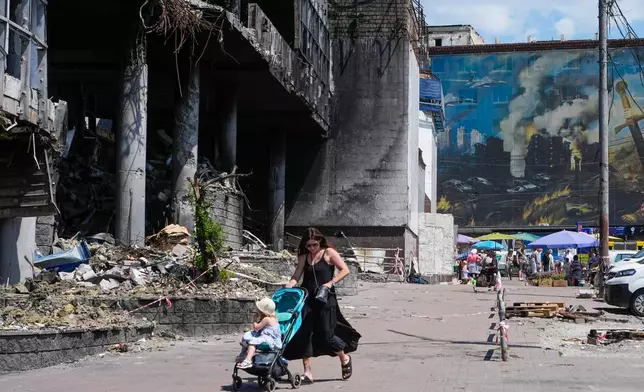 A mother pushes a stroller past a damaged building covered with street artist paintings and a big city marketplace that was destroyed recently by Russian missiles in Kyiv, Ukraine, Monday, June 22, 2026. (AP Photo/Efrem Lukatsky)