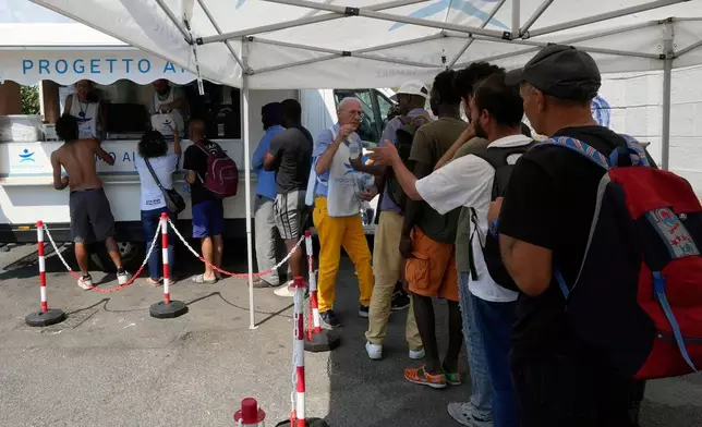 FILE - Volunteers distribute food and water to homeless people at the Progetto Arca Onlus foundation volunteer shelter, in Milan, Italy, July 3, 2025. (AP Photo/Luca Bruno, File)