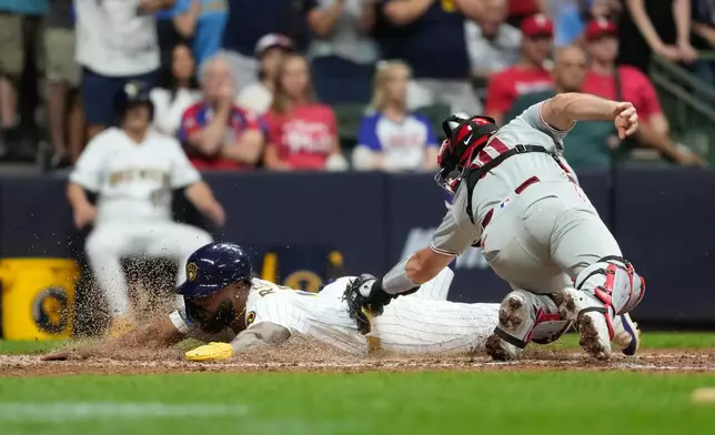 Milwaukee Brewers' Luis Rengifo slides past Philadelphia Phillies' J.T. Realmuto to score a run during the eighth inning of a baseball game Saturday, June 13, 2026, in Milwaukee. (AP Photo/Aaron Gash)