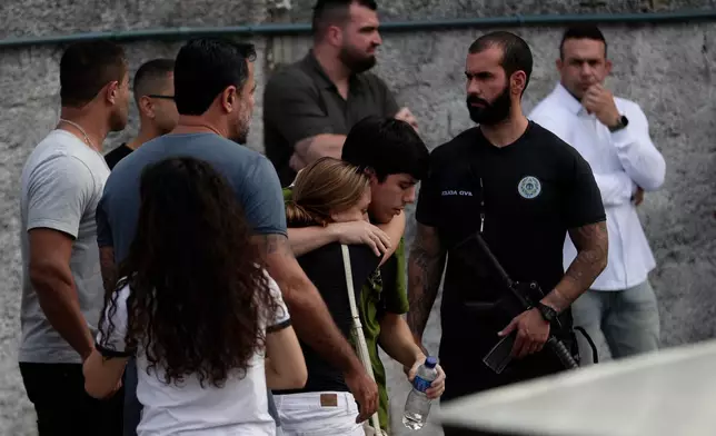 People comfort each other near the site where two helicopters reportedly collided in midair and crashed into a car dealership parking lot in Rio de Janeiro, Brazil, Sunday, June 14, 2026. (AP Photo/Bruna Prado)