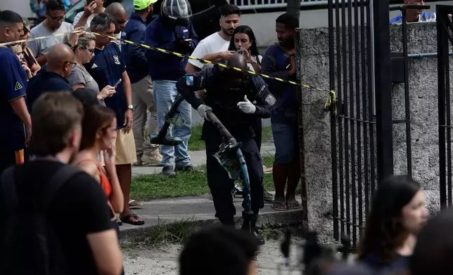 A police officer carries debris at the site where two helicopters reportedly collided in midair and crashed into a car dealership parking lot in Rio de Janeiro, Brazil, Sunday, June 14, 2026. (AP Photo/Bruna Prado)