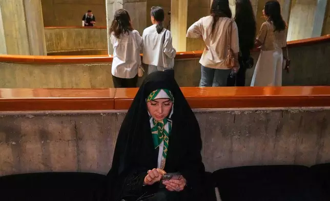 A woman checks her cellphone as visitors attend "A Sign on Minab," an event honoring the memory of schoolchildren killed in a Feb. 28, 2026, strike on a school in the southern Iranian city of Minab that was likely caused by U.S. airstrikes, at the Tehran Museum of Contemporary Art in Tehran, Iran, Sunday, June 14, 2026. (AP Photo/Vahid Salemi)