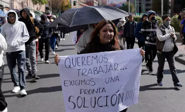 A vendor carries a sign reading in Spanish "We want to work, we demand a prompt solution," during a march against protesters who are blocking access to La Paz, Bolivia, Monday, June 8, 2026. (AP Photo/Juan Karita)