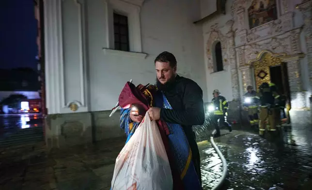A priest carries church inventory out of the burning Dormition Cathedral of the Kyiv-Pechersk Lavra, also known as the Monastery of the Caves, during a Russian strike on Kyiv, Ukraine, on Monday, June 15, 2026. (AP Photo/Evgeniy Maloletka)