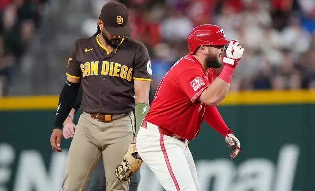Texas Rangers' Jake Burger, right, reacts in front of San Diego Padres second baseman Fernando Tatis Jr. after hitting an RBI double to score Alejandro Osuna and Ezequiel Duran during the first inning of a baseball game, Friday, June 19, 2026 in Arlington, Texas. (AP Photo/Julio Cortez)