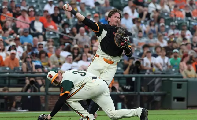 Baltimore Orioles catcher Adley Rutschman throws to first base for an out as pitcher Shane Baz ducks on a ball hit by San Diego Padres' Manny MacHado during the second inning of a baseball game, Friday, June 12, 2026, in Baltimore. (AP Photo/Terrance Williams)