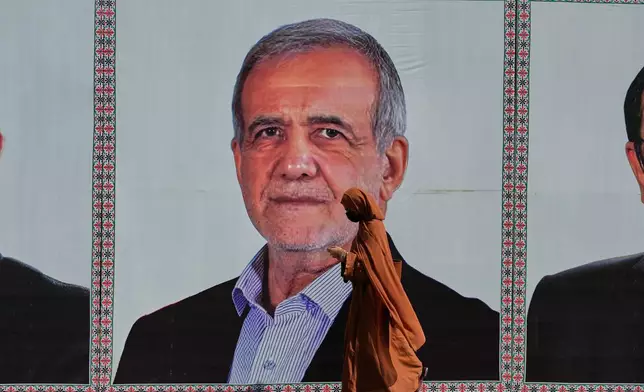 A woman walks past a welcoming billboard featuring Iranian President Masoud Pezeshkian along a roadside in Islamabad, Pakistan, Tuesday, June 23, 2026. (AP Photo/Anjum Naveed)