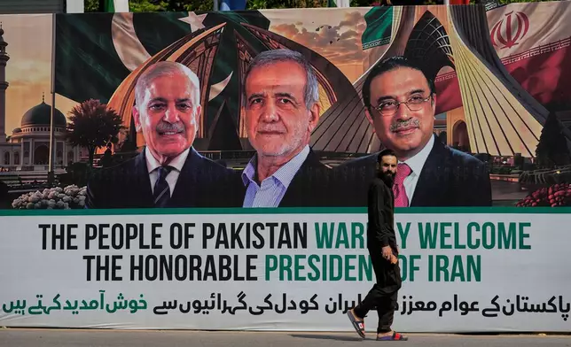 A man walks past a welcoming billboard featuring Iranian President Masoud Pezeshkian, center, with Pakistan President Asif Ali Zardari, right, and Shehbaz Sharif along a roadside in Islamabad, Pakistan, Tuesday, June 23, 2026. (AP Photo/Anjum Naveed)
