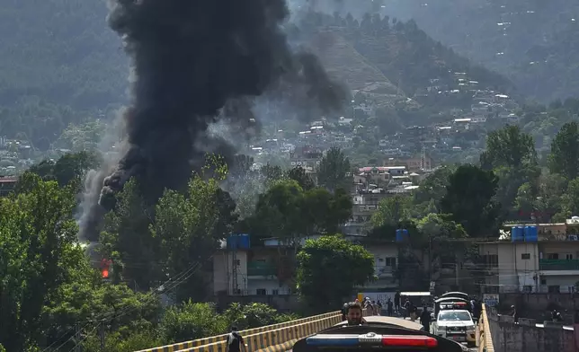A police vehicle is parked at along a road as smoke billows after an army MI-17 helicopter crashed due to a technical fault, in Muzaffarabad, capital of Pakistan-administered Kashmir, Wednesday, June 10, 2026. (AP Photo/M.D. Mughal)