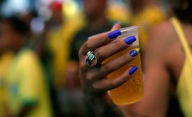 FILE - A soccer fan, with nails painted with a Brazil flag, holds a beer while watching the team's World Cup match against Serbia on a screen set up in the Rocinha favela in Rio de Janeiro, Brazil, Nov. 24, 2022. (AP Photo/Bruna Prado, File)