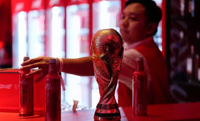 FILE - A bartender clears bottles of Budweiser beer from the bar near a replica of the FIFA World Cup trophy at an official U.S. Soccer fan party at the Budweiser World Club, in Doha, Qatar, Nov. 20, 2022. (AP Photo/Ashley Landis, File)