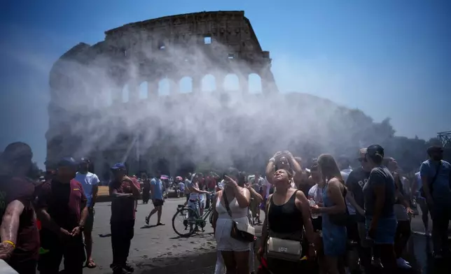 People refresh in front of a water-sprinkling cannon brought by Rome's municipality to relieve tourists visiting the Colosseum and Roman Forum as temperatures reach record highs, in Rome, Friday, June 26, 2026. (AP Photo/Andrew Medichini)