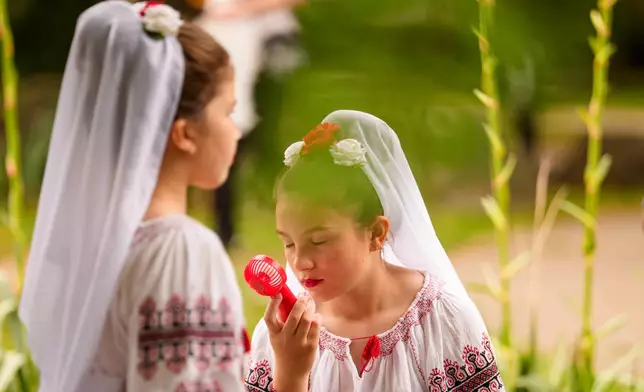 A girl wearing a traditional outfit uses a hand held battery powered fan to cool down on a hot day during an event marking summer solstice at the Dimitrie Gusti Village Museum in Bucharest, Romania, Wednesday, June 24, 2026. (AP Photo/Andreea Alexandru)