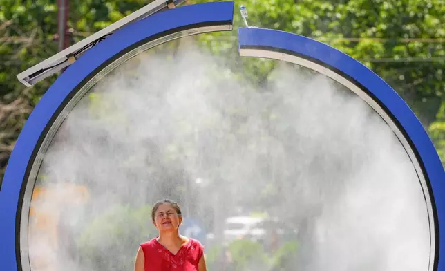 A woman cools off in a water mist machine installed by city administration to assist people in coping with the heat on a torrid day, as the National Weather forecaster issued an extreme heat code red warning for most parts of the country, in Bucharest, Romania, Monday, June 29, 2026. (AP Photo/Vadim Ghirda)