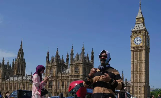 A man shelters from the sun as he crosses Westminster Bridge as a heat wave is predicted in London, Tuesday, June 23, 2026. (AP Photo/Kirsty Wigglesworth)