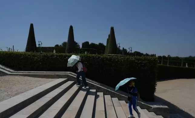 Visitors shield themself from the sun with umbrellas as they walk in the garden of the Palace of Versailles, outside Paris, during a heat wave with temperatures soaring above 40 degrees Celsius (104 Fahrenheit), Monday, June 22, 2026. (AP Photo/Thibault Camus)