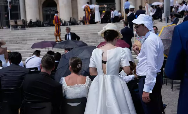 Newly couple of spouses shelter for the hot sun as they wait to meet Pope Leo's XIV during his weekly general audience in St. Peter's Square at The Vatican, Wednesday, June 24, 2026. (AP Photo/Alessandra Tarantino)