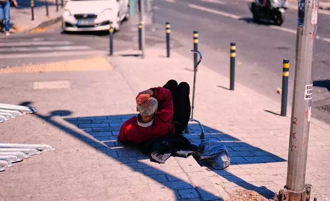 A man takes shelter in the shade of a street board to protect himself from the sun in Istanbul, Turkey, Wednesday, June 24, 2026. (AP Photo/Francisco Seco)