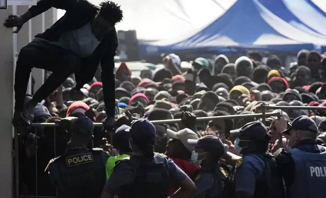 A Malawian migrant jumps over a barricade as the police officer manage the queue for their deportation at a temporary centre, in Durban, South Africa, Thursday, June 18, 2026. (AP Photo/Themba Hadebe)