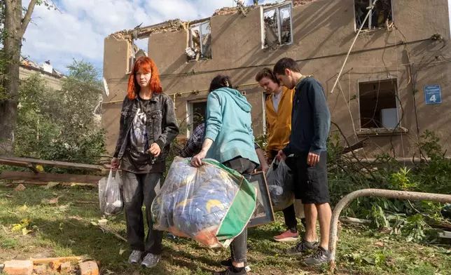 People carry their belongings as they leave their home after a Russian missile hit a residential building during an air attack in Kharkiv, Ukraine, Saturday, June 20, 2026. (AP Photo/Andrii Marienko)