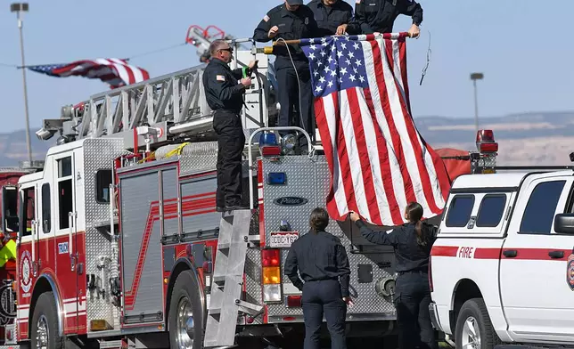 Firefighters with the Lower Valley Fire Protection District hang an American flag along a procession route in honor of three firefighters killed while fighting the Snyder Fire in Grand Junction, Colo. Sunday, June 28, 2026. (Gretel Daugherty via AP)
