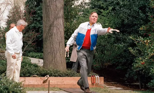FILE - President George H.W. Bush lets loose of a horseshoe during the dedication of the new horseshoe pit on the White House lawn Saturday April 1, 1989, in Washington. (AP Photo/Barry Thumma)