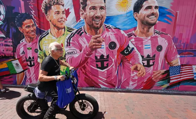 A man rides a bike past a new mural by artist Disem featuring Inter Miami players competing for their national teams in the 2026 World Cup, in Miami's Little Havana neighborhood, Wednesday, June 17, 2026. Pictured, from right, are Rodrigo De Paul and Lionel Messi of Argentina, Dayne St. Clair of Canada, and Ian Fray of Jamaica. (AP Photo/Rebecca Blackwell)