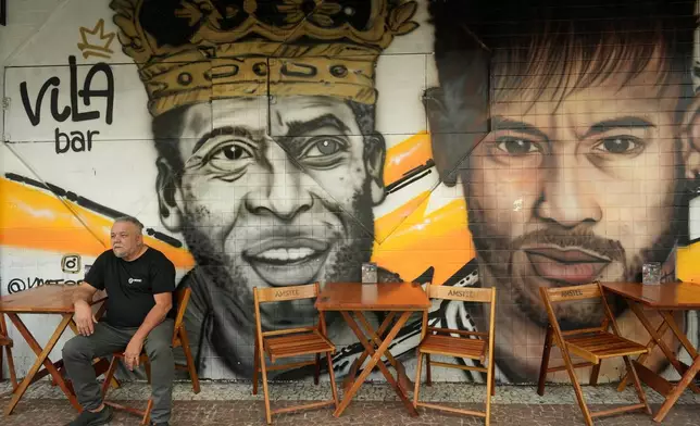 A man sits in front of a mural of late football legend Pele and Neymar at a restaurant in Santos, Brazil, Thursday, May 28, 2026. (AP Photo/Andre Penner)