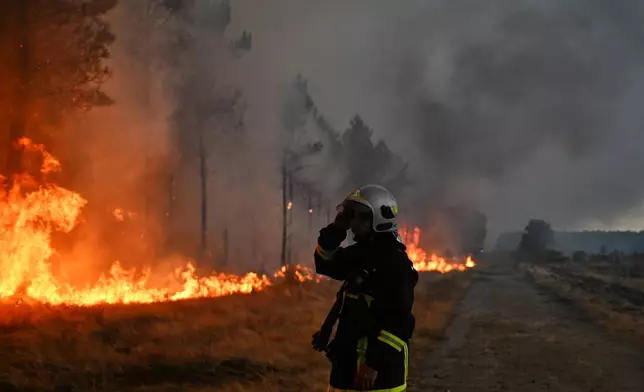 A firefighter gestures next to burning trees as a wildfire rages near Marcheprime, outside, Bordeaux, France, Sunday, July 26, 2026. (AP Photo/Emma Da Silva)