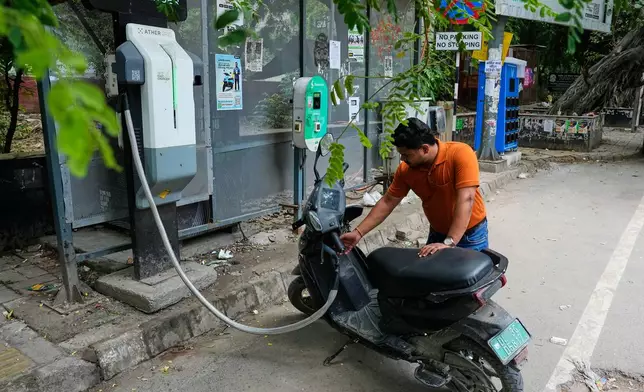 A person charges his electric scooter at a roadside charging station in New Delhi, India, Monday, July 13, 2026. (AP Photo/Manish Swarup)