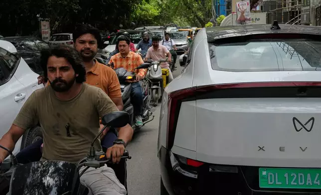 Two wheelers drive past an electric vehicle parked along a street in New Delhi, India, Monday, July 13, 2026. (AP Photo/Manish Swarup)
