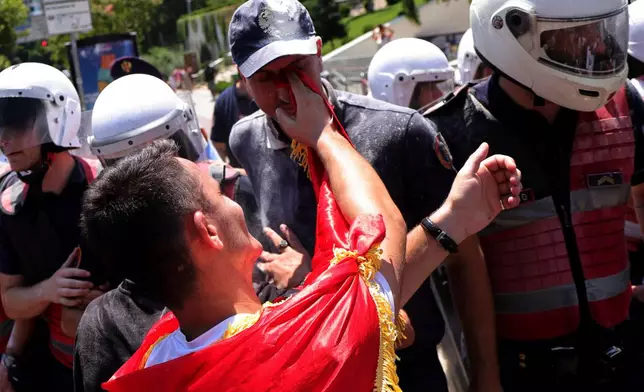 A protester uses a flag to wipe flour from a police officer's face during clashes at an anti-government rally in Tirana, Albania, Thursday, July 2, 2026. (AP Photo/Hameraldi Agolli)
