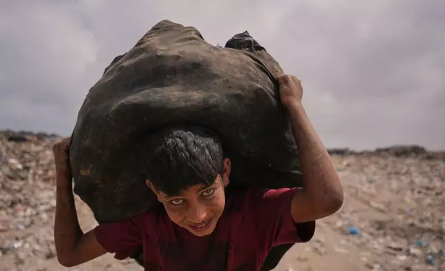 Omar Ghabin, 14, looks at the camera as he carries a bag of items he collected from the landfill in Deir al-Balah, central Gaza Strip, Thursday, July 23, 2026. (AP Photo/Abdel Kareem Hana)