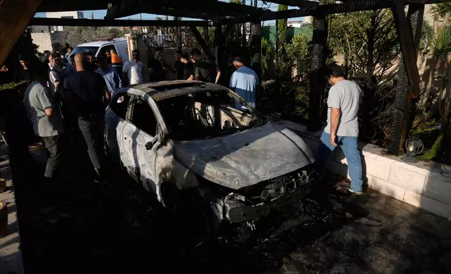 Palestinians stand next to a burned car following an attack by Israeli settlers in the village of Sarra, near the West Bank city of Nablus, Friday, July 24, 2026. (AP Photo/Majdi Mohammed)