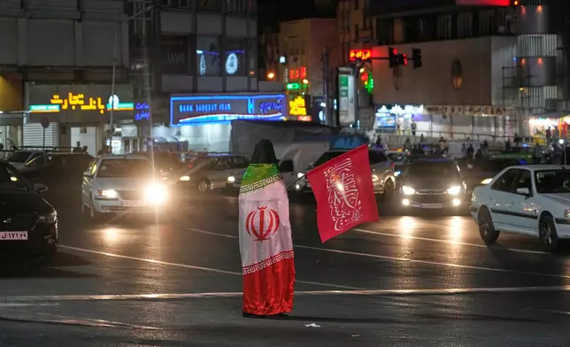 A pro-government demonstrator wears an Iranian flag as she holds a religious flag in a gathering commemorating the late Iranian Supreme Leader Ayatollah Ali Khamenei at a square in Tehran, Iran, Saturday, July 11, 2026. (AP Photo/Vahid Salemi)