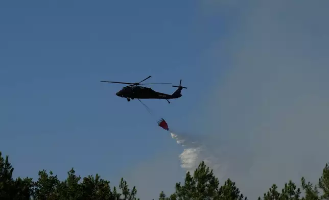An Blackhawk helicopter lets a Bambi Bucket full of water go over a firezone near Lacanau, as wildfires rage outside Bordeaux, France, Monday, July 27, 2026. (AP Photo/Baz Ratner)