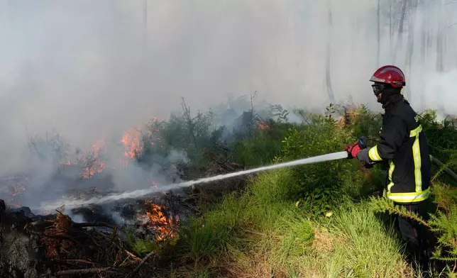 A firefighter works to suppress flames near Lacanau, as wildfires rage outside Bordeaux, France, Monday, July 27, 2026. (AP Photo/Baz Ratner)
