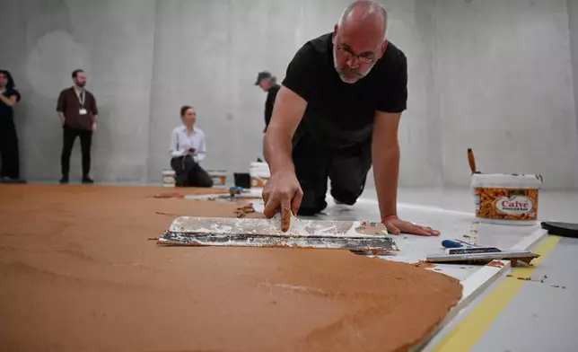 Workers spread peanut butter on a floor to recreate the "Peanut Butter Floor" artwork in tribute to Dutch artist Wim T. Schippers at the Museum Boijmans Van Beuningen in Rotterdam, Netherlands, Friday, July 3, 2026. (AP Photo/Mouneb Taim)